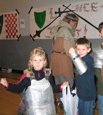 Several little kids in a row wearing various medieval metal armor on loan from the Society for Creative Anachronism